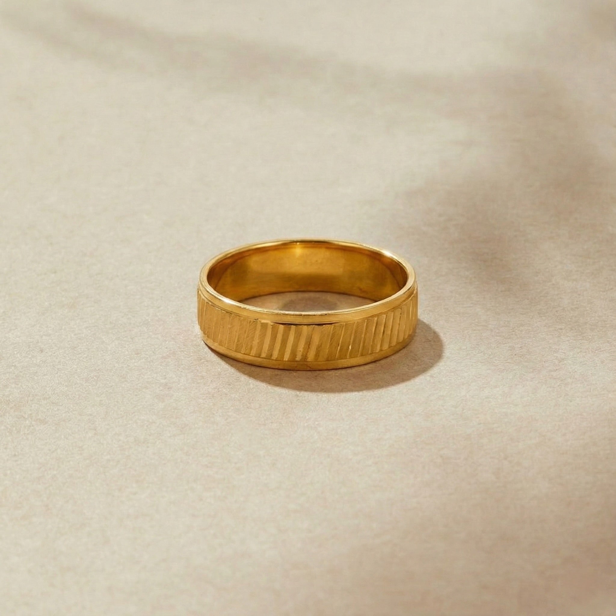 Gold ring with a textured band on a beige background