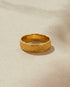 Gold ring with a textured band on a beige background