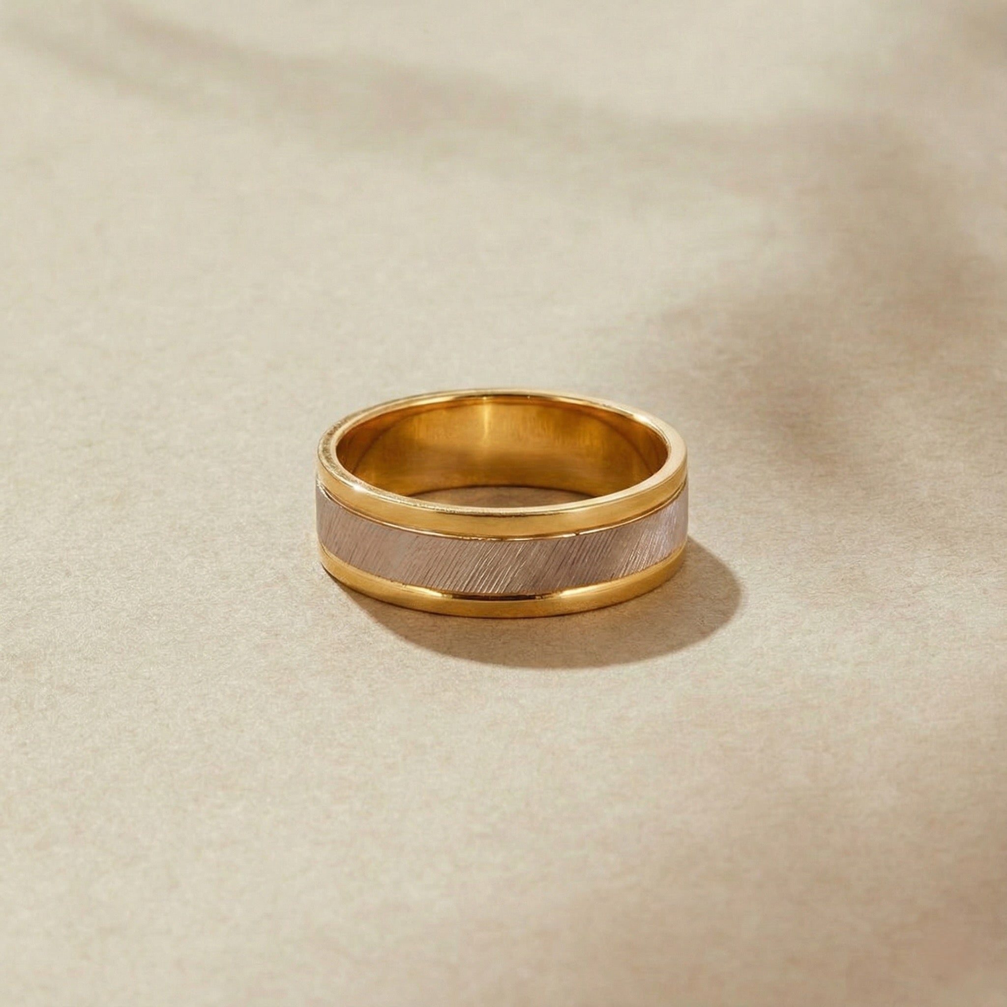 Gold ring with a textured band on a beige background