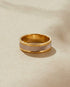 Gold ring with a textured band on a beige background