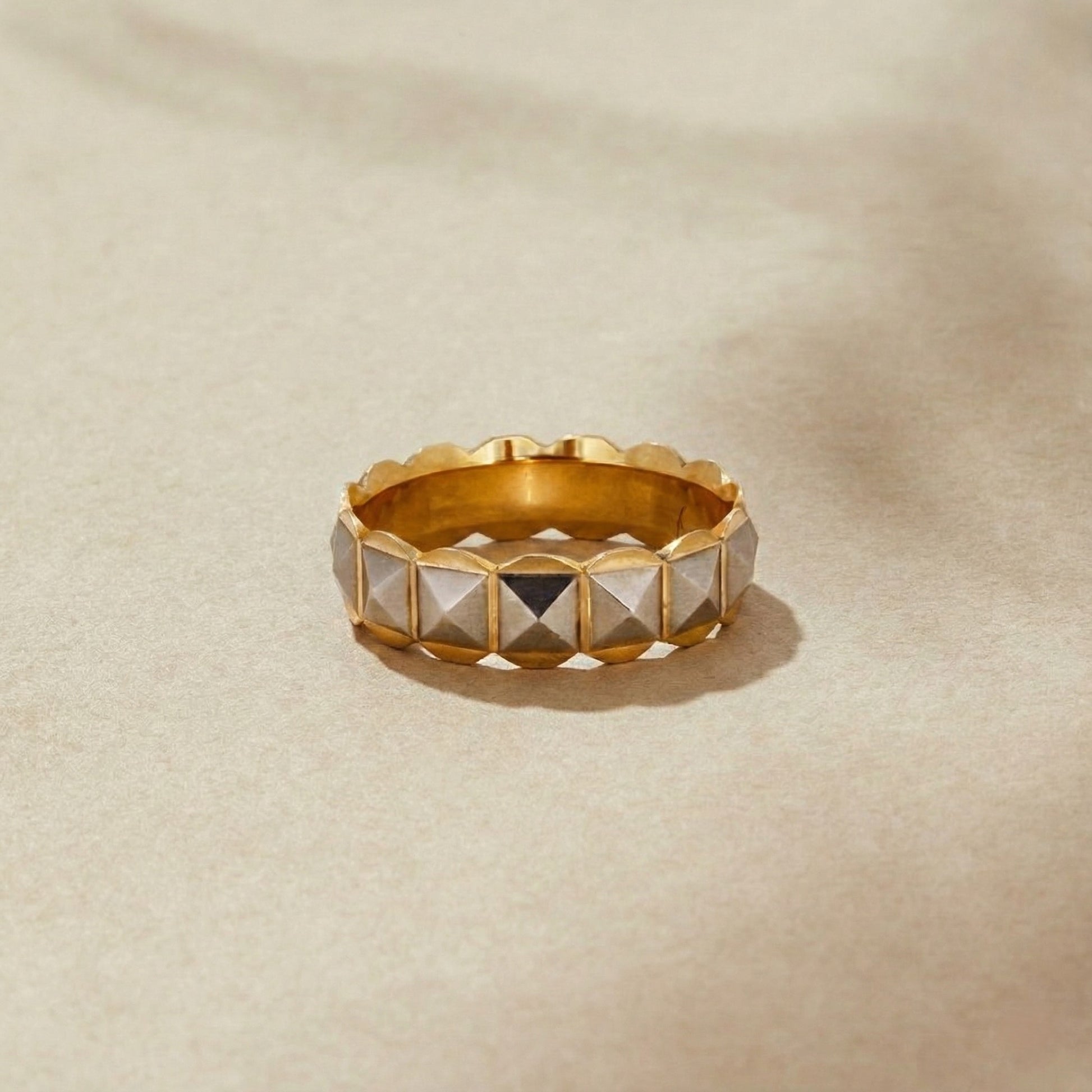 Gold ring with pyramid-shaped stones on a beige background